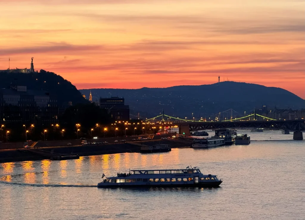 Sunset view over the Danube in Budapest with a sightseeing boat cruising past the riverfront lights and bridges, perfect for a private sightseeing cruise photo.