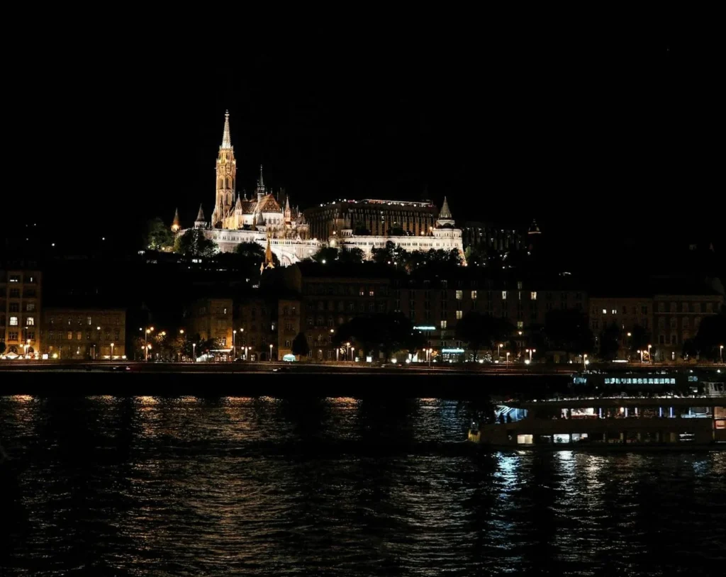 Illuminated Buda Castle and Matthias Church seen from a boat on the Danube at night, showing how Budapest’s evening lights shape the best cruise time and season choice.