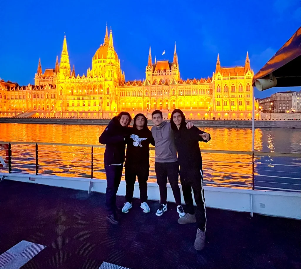 Stag group photo on a boat in Budapest at night, with the Hungarian Parliament glowing across the Danube in the background.